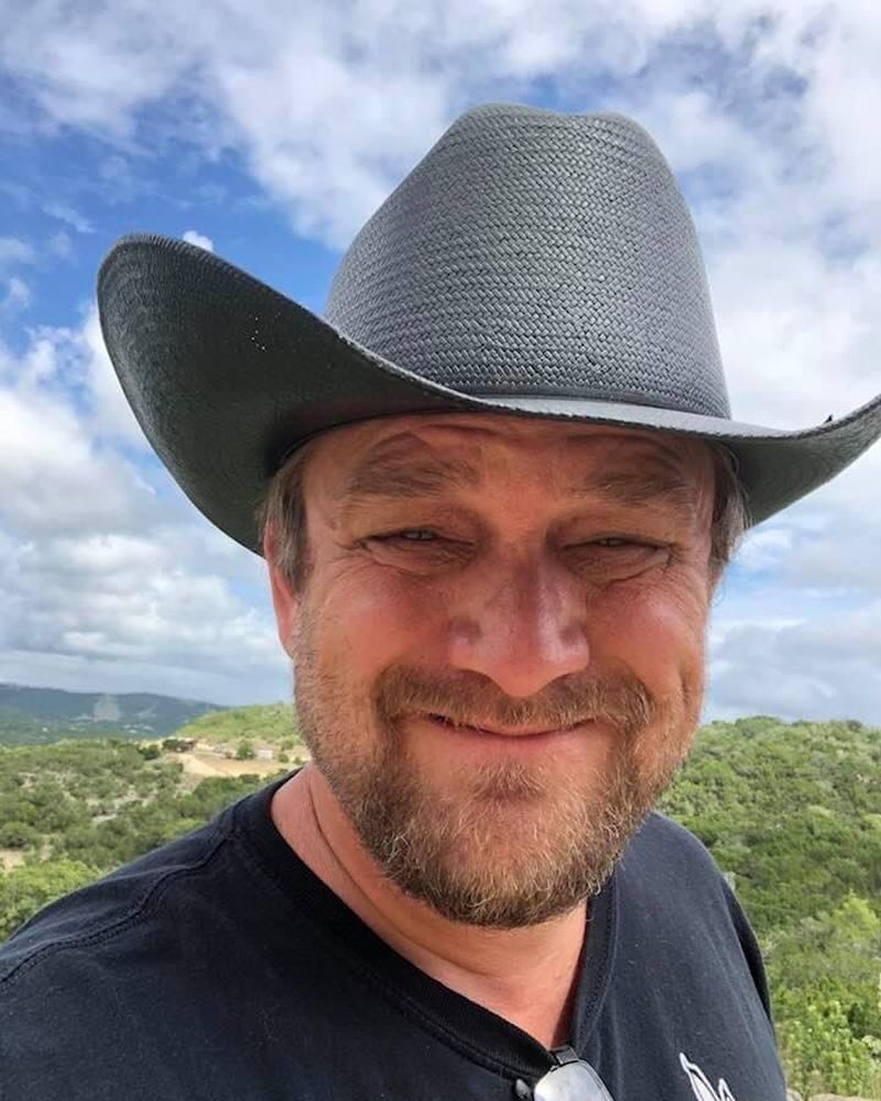 Spencer Forrest in a black straw cowboy hat, Hill Country hills behind him